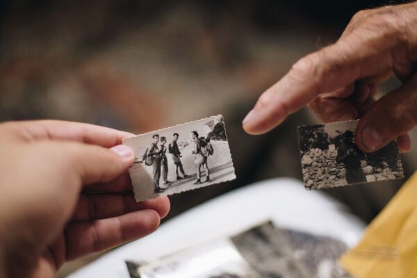 A younger hand holds a small black-and-white photo while an older hand points at another old photo