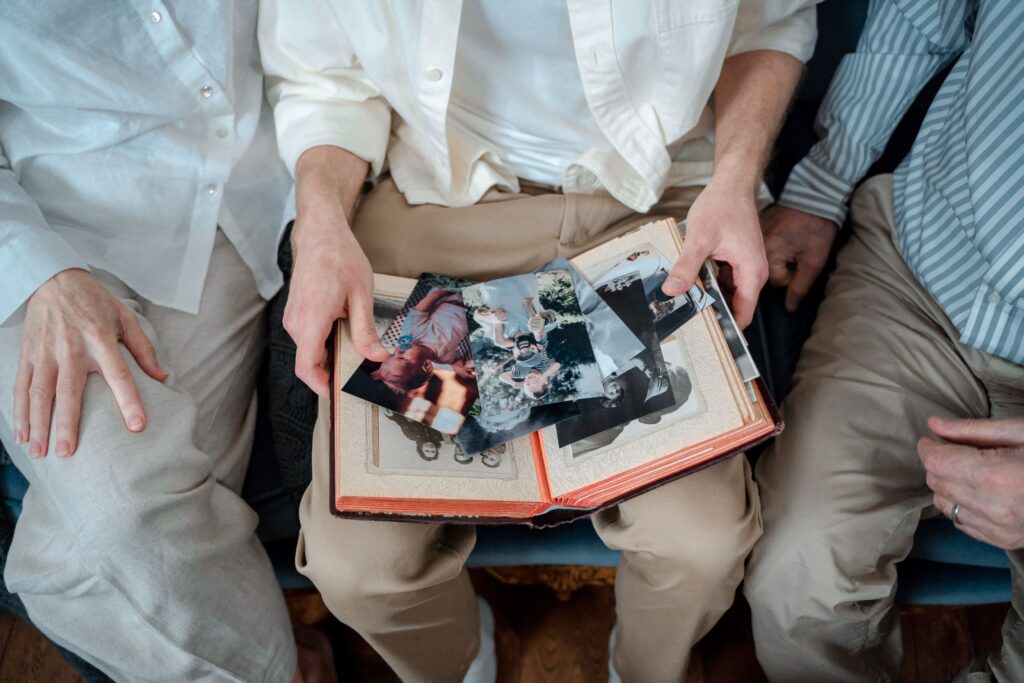 Three family members' hands on an open photo album full of old colour and black-and-white prints
