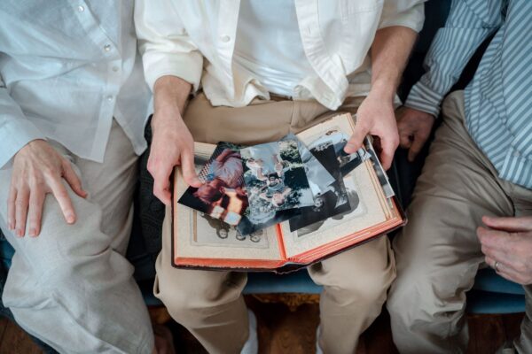 Three family members' hands on an open photo album full of old colour and black-and-white prints